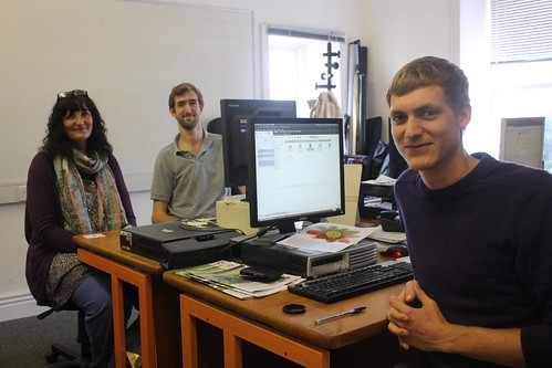 Nicola, Tom and John sit desks in the office