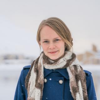 Hildur standing in a wintercoat, with a knitted scarf, in front of snowy town of Ísafjörður