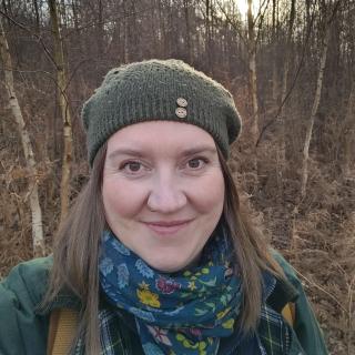 Emma is standing in her favourite wood of Silver Birches wearing a cosy hat and scarf.