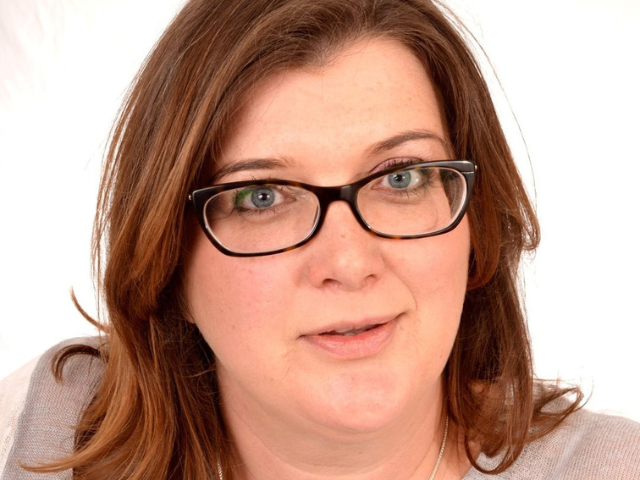 Image of a white woman with long brown hair and glasses smiling. 