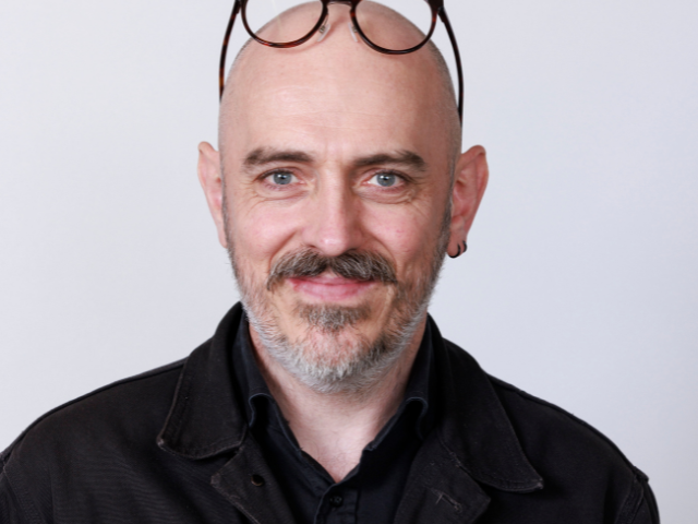 Image of a man with a moustache and beard with glasses on his head. 
