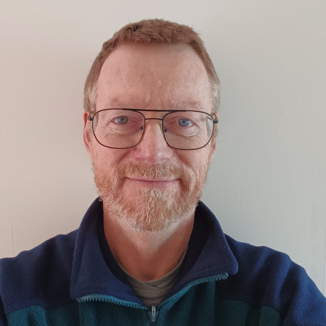A picture of a man with glasses, short hair and a beard smiling. He is wearing a blue fleece. 
